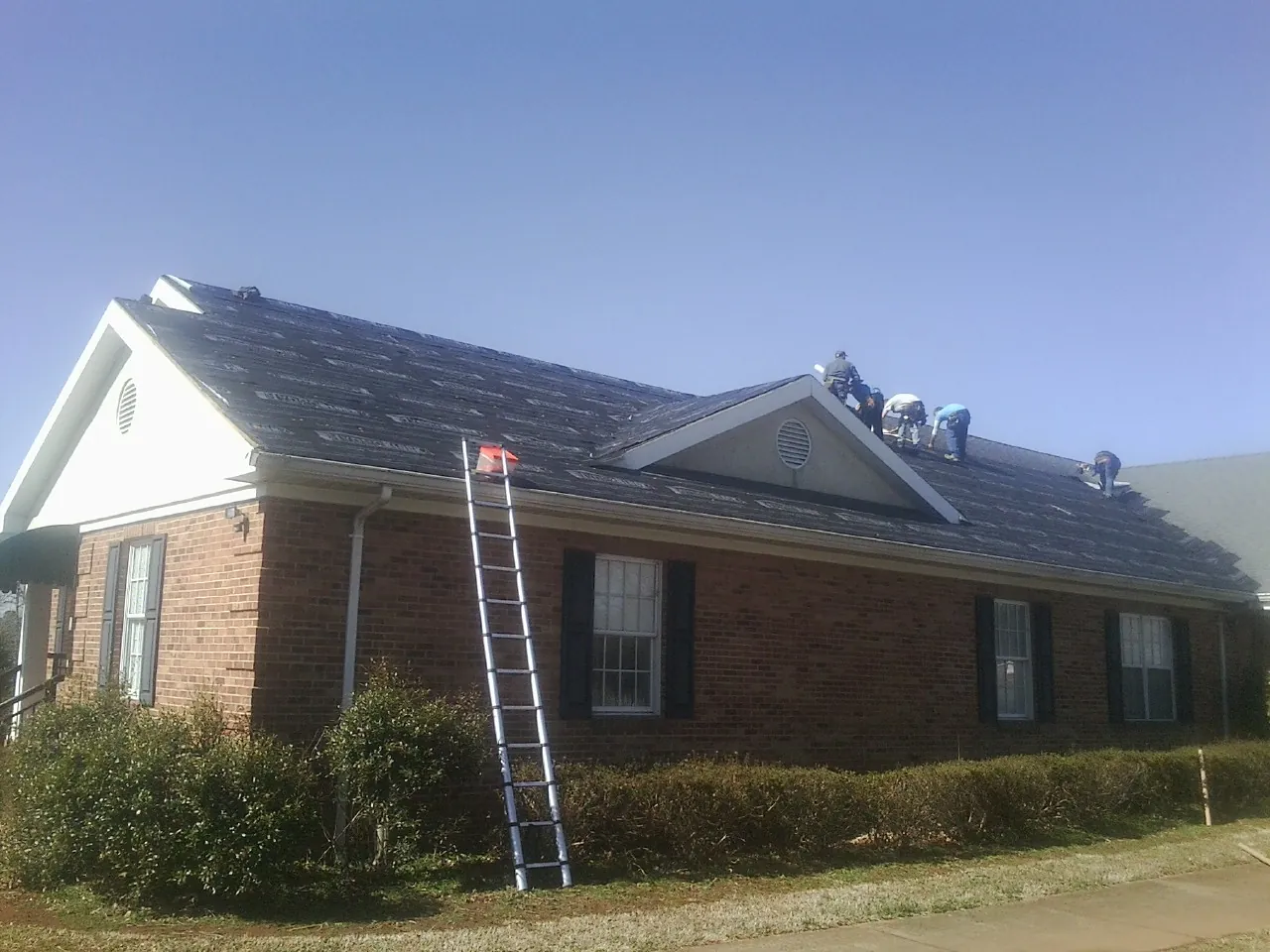 Crew tearing shingles off a brick ranch roof with a ladder set — Metal Roof Repair work by our crew in Laketon