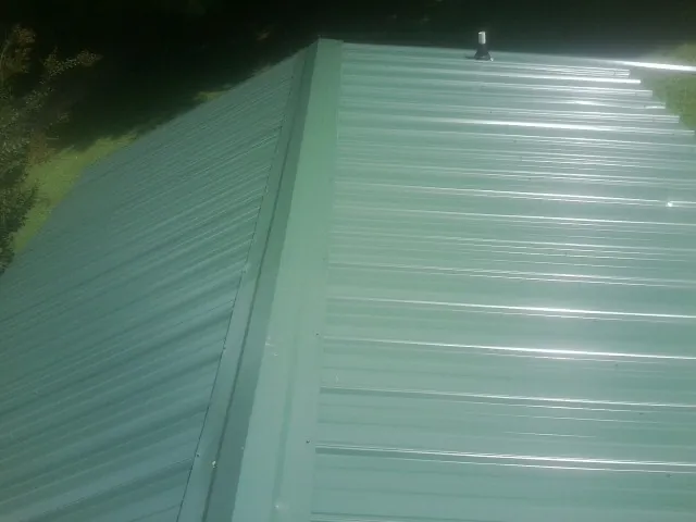 New green metal panels meeting at the ridge of a roof — Flat Roof Repair work by our crew in Laketon