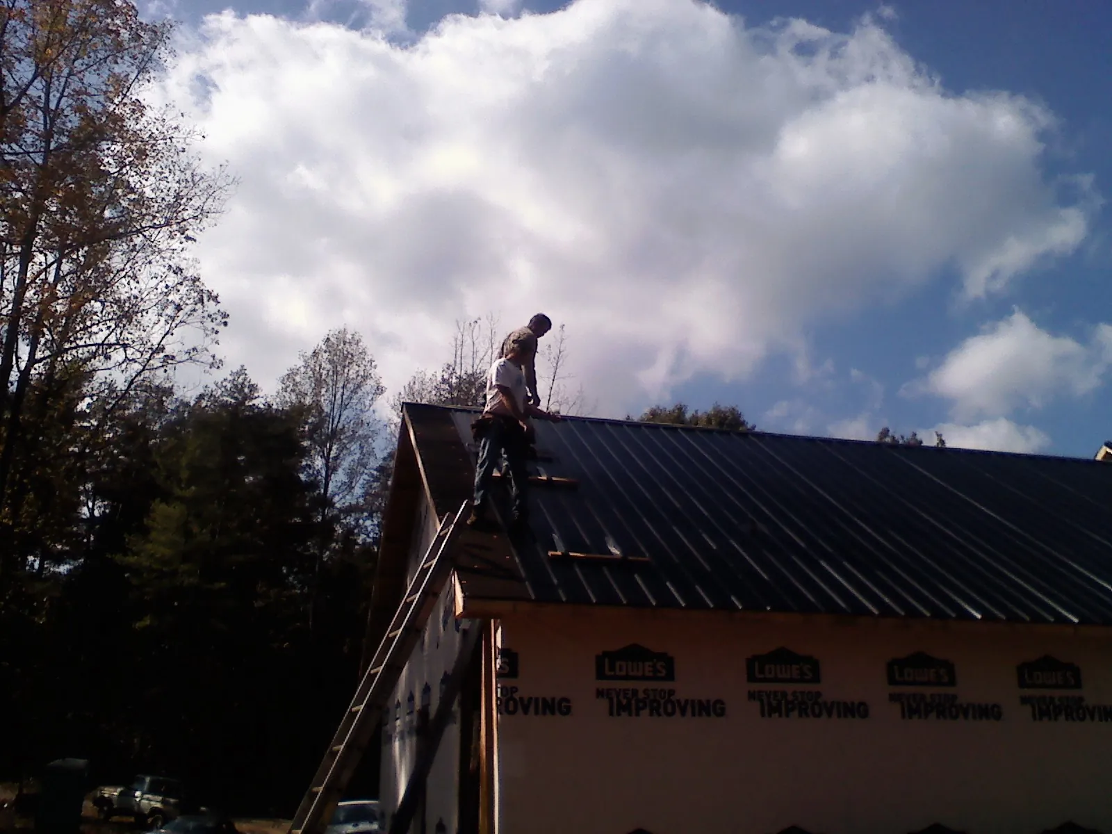 Roofer fastening dark metal panels high against a cloudy sky, from a Roof Inspection job in Laketon