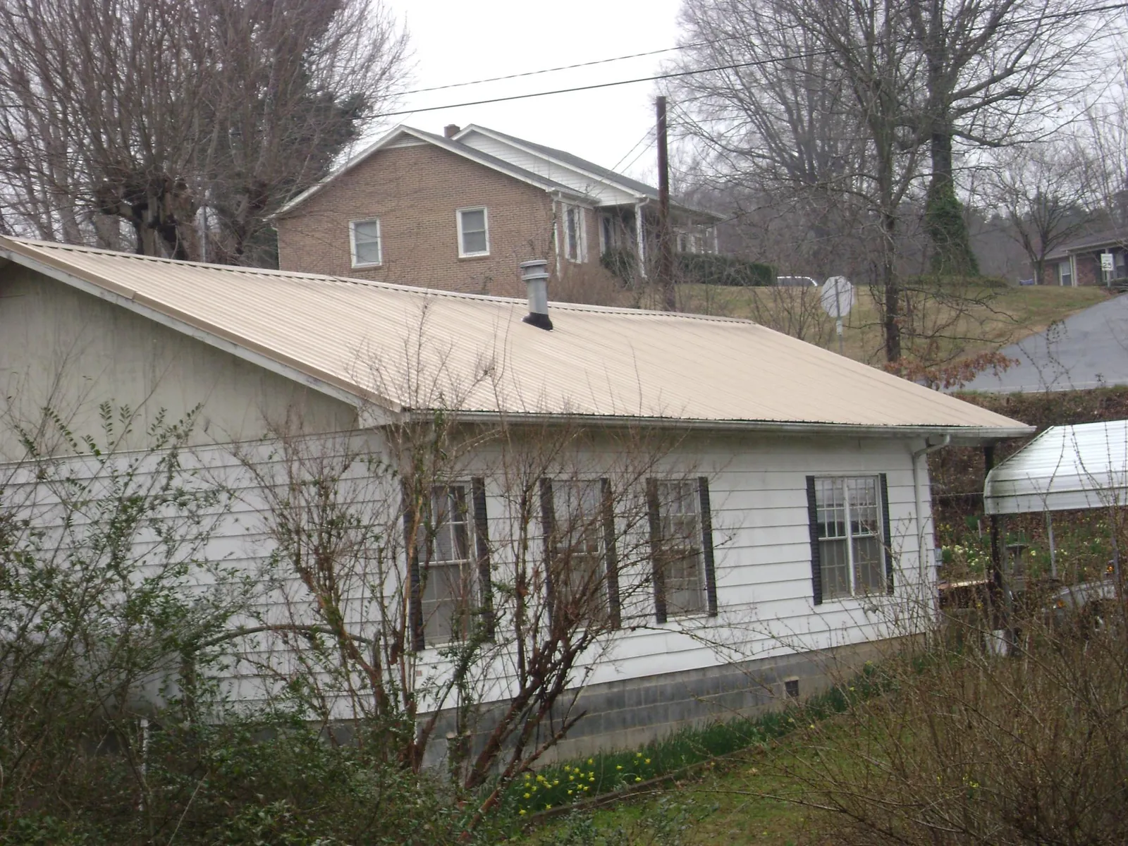 Tan metal roof on a white sided house set into a hillside — Commercial Roofing by Roofing Brothers in Laketon
